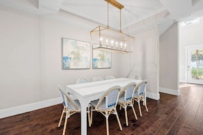 A dining area with a white table and wicker chairs, a chandelier, and abstract wall art. - Sea Rest | Private Pool | Deeded Beach Access | 3 King Suites (Watersound Beach)