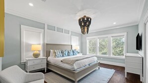 Un dormitorio con cama, mesitas de noche, una silla, un candelabro y una ventana.