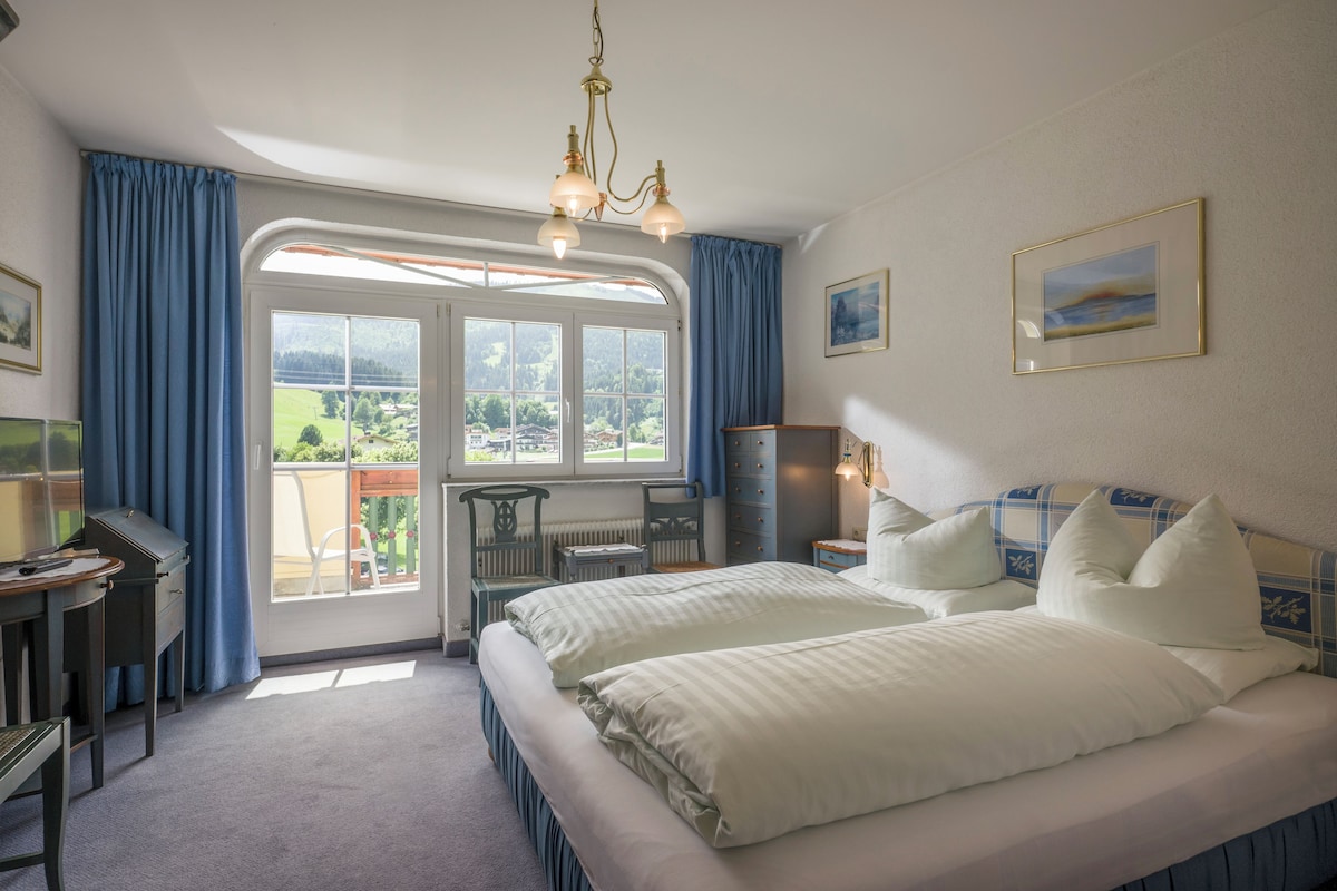 A hotel room with a bed, a desk, a chair, a dresser, and a view of the outdoors.