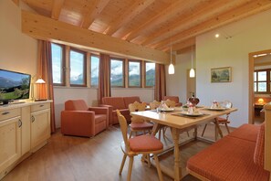 A cozy room with wooden beams, a dining table set for two, and a television displaying a mountainous landscape.
