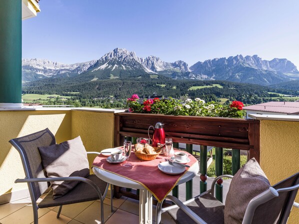 A balcony with a table set for two, overlooking a mountainous landscape.