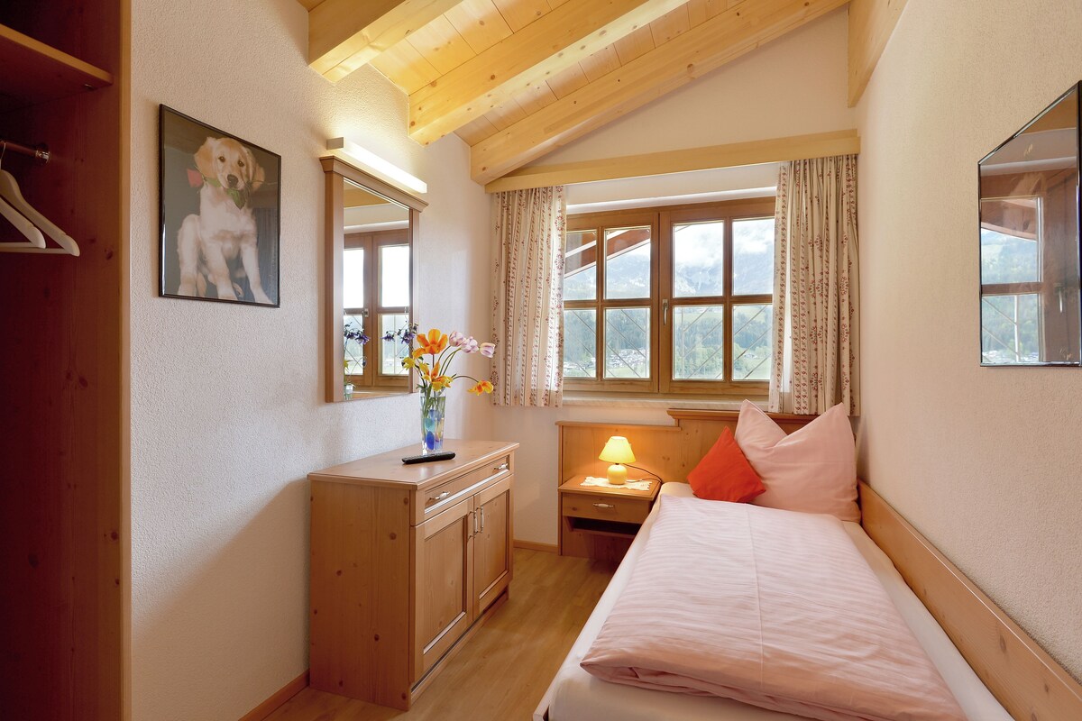 A bedroom with a bed, a nightstand, a dresser, a mirror, a window with curtains, and a painting on the wall.