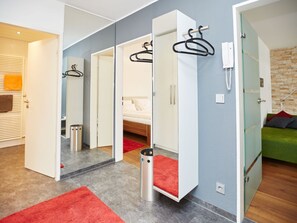 A modern hotel room with a bed, a red rug, a trash bin, and a mirror with a hanging coat rack. - Alpenflair Holiday Apartment 213 "timeless" (Oberstdorf)