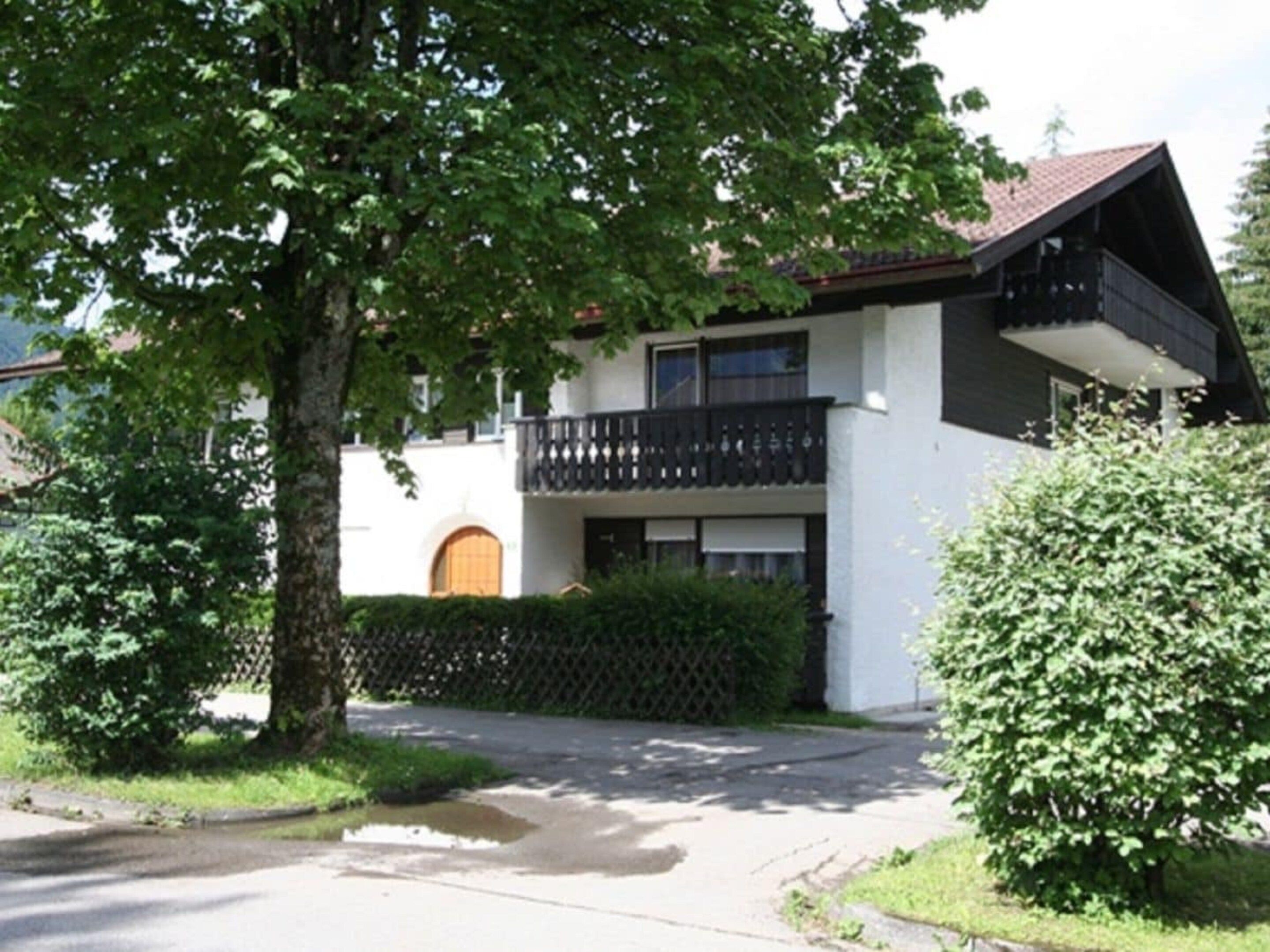 A two-story building with a balcony, a gated entrance, and a tree in the foreground.