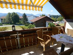 A balcony with wicker furniture, a table with a lace tablecloth, and a view of houses and mountains. - 3 - Ellen Raith (Fuessen)