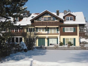 A multi-story building with a balcony, a garage, and a snow-covered ground. - 3 - Ellen Raith (Fuessen)