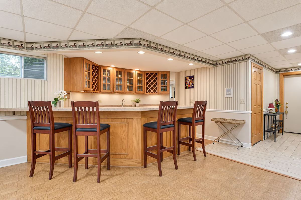 Una cocina con armarios de madera, una zona de bar con taburetes y piso de baldosas.