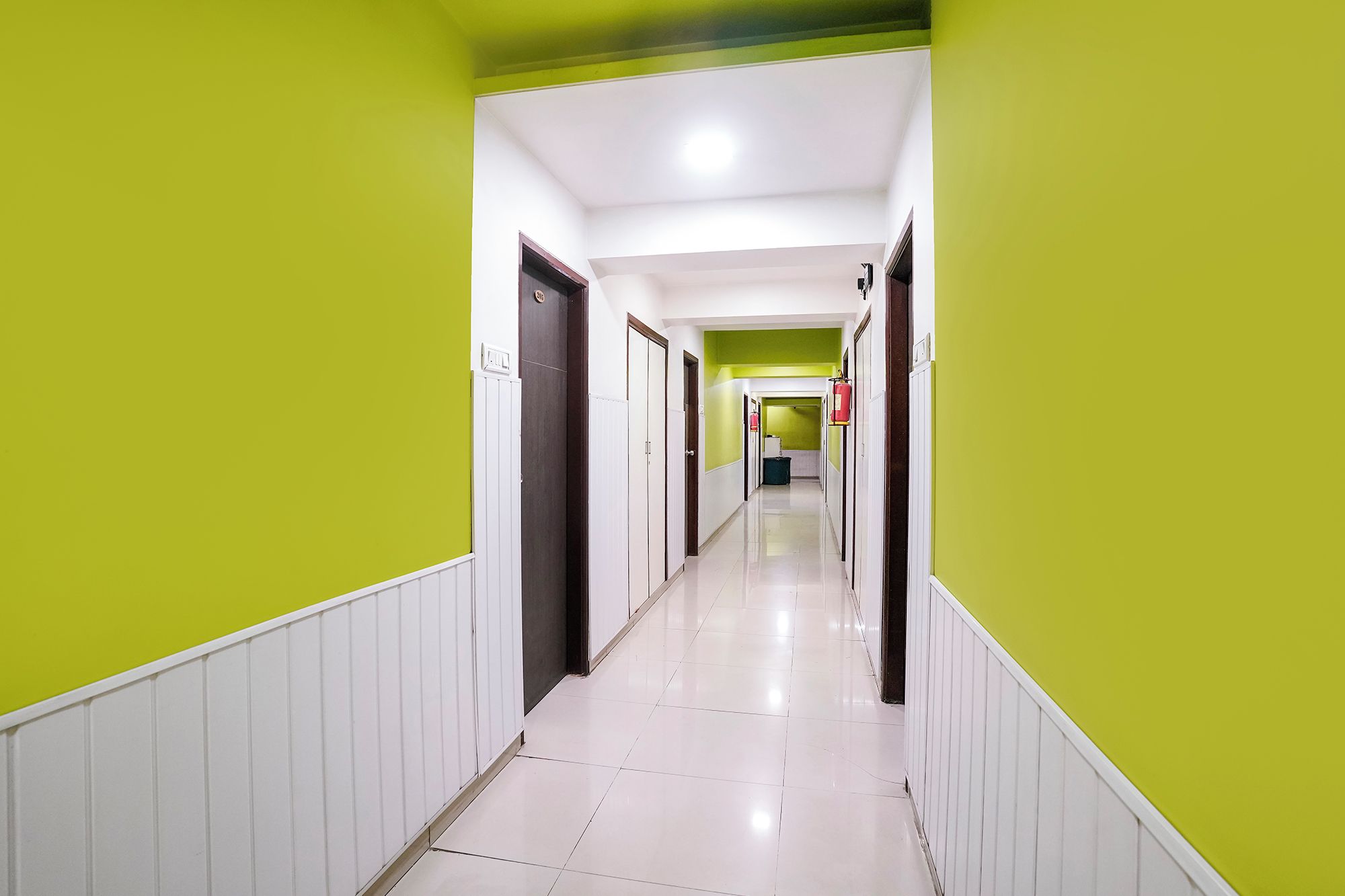 A corridor with doors on both sides, leading to a room with a green wall and a white ceiling.