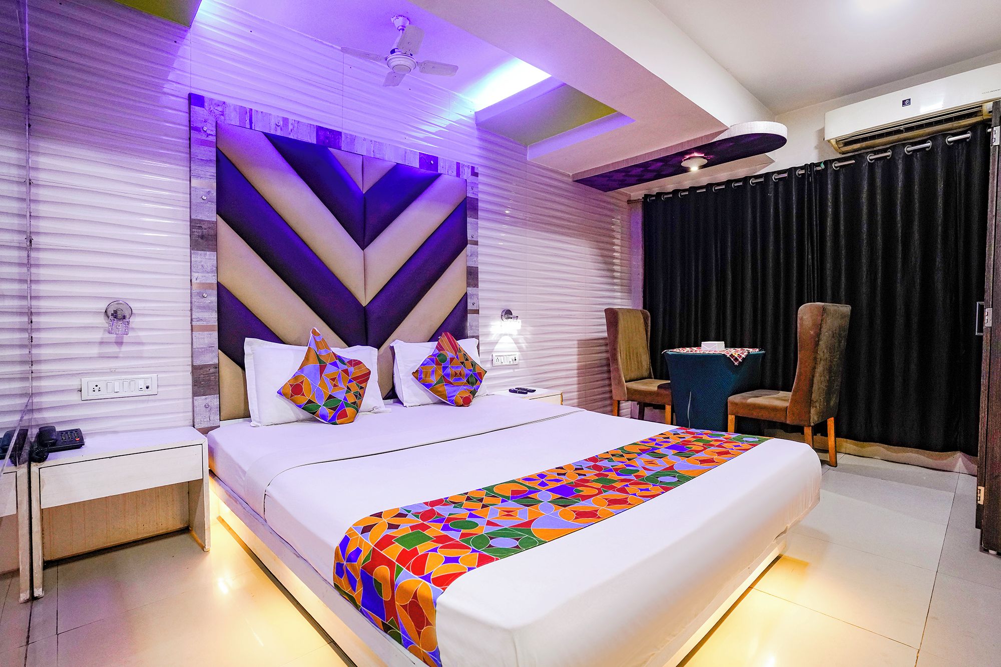 A modern hotel room with a large bed, a desk, a chair, and a ceiling fan.