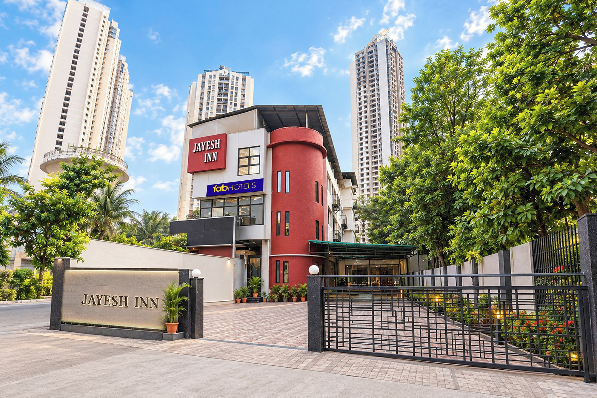 A hotel entrance with a gated driveway, a sign for 'Jayesh Inn,' and a 'Fab Hotels' sign.