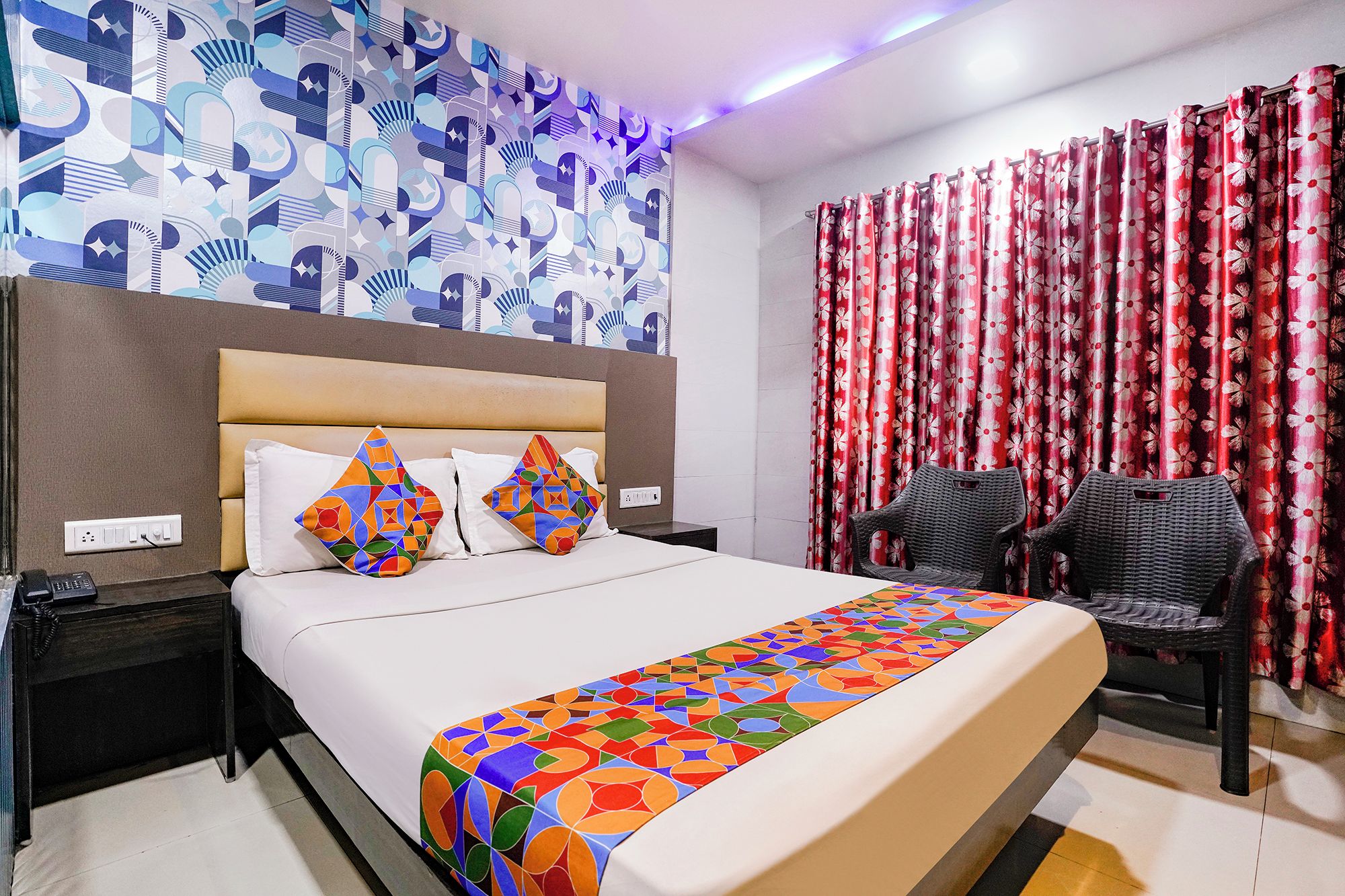 Habitación de hotel con cama, mesitas de noche, teléfono, cabecera, pared con estampado y ventana con cortinas.