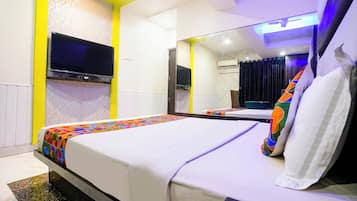 A hotel room with a bed, a flat-screen TV mounted on the wall, a mirror, and a ceiling fan.