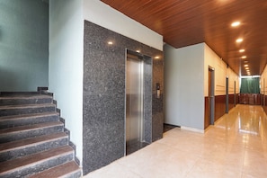 A modern interior with a marble elevator, a staircase, and a hallway with doors.