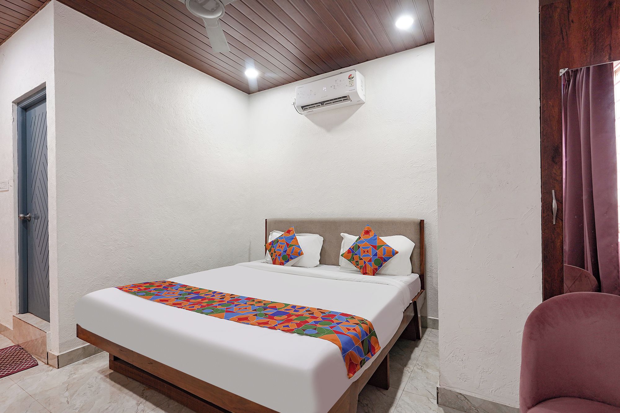 Una habitación de hotel con una cama, un ventilador de techo, un equipo de aire acondicionado y una puerta.