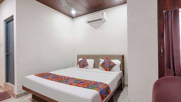 Una habitación de hotel con una cama, un ventilador de techo, un equipo de aire acondicionado y una puerta.