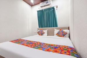 A hotel room with a bed, a window with curtains, and an air conditioning unit.