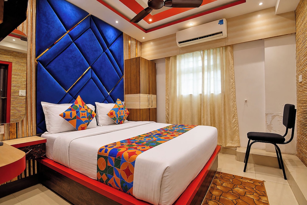 A modern hotel room with a large bed, a red accent wall, and a ceiling fan.