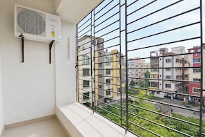 A balcony with a metal railing, an air conditioning unit, and a view of multi-story buildings. - FabHotel Love Point (Barasat)