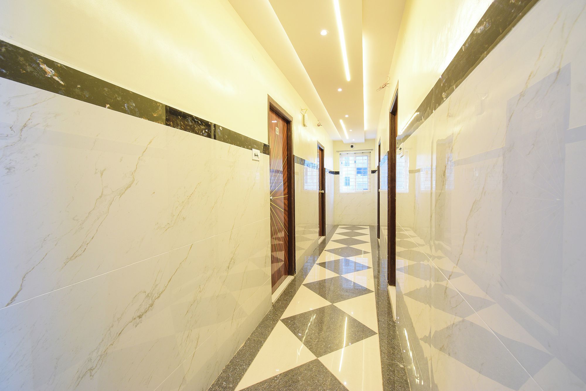 Corredor de hotel com paredes de mármore, piso xadrez e portas que dão para os quartos.