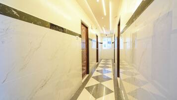 Corredor de hotel com paredes de mármore, piso xadrez e portas que dão para os quartos.