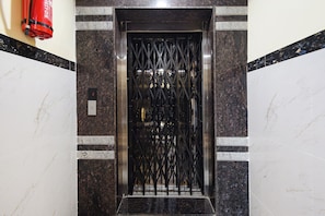 An elevator with a metal gate, marble walls, and a fire extinguisher on the left. - FabHotel Dream Pride (Hyderabad)