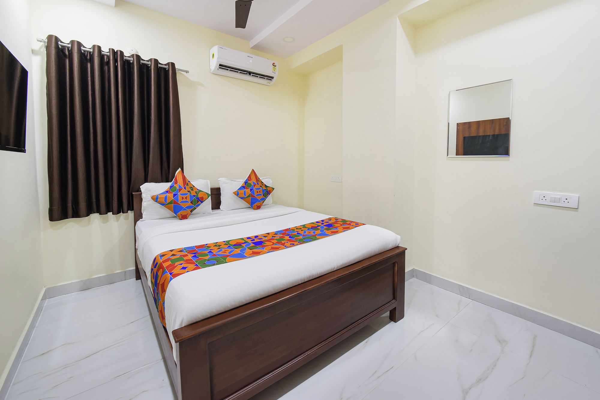 Una habitación de hotel con cama, ventilador de techo, aire acondicionado, espejo y toma de corriente.