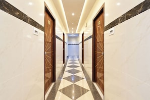Un pasillo de hotel con paredes de mármol, piso a cuadros y puertas de madera con números.