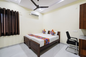 Habitación de hotel con cama, ventilador de techo, aire acondicionado, escritorio y una silla.