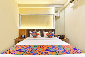 A hotel room with a bed, a nightstand, a bedside table, a pillow, a blanket, and a wall-mounted air conditioning unit. - FabHotel The Samsara (Ujjain)