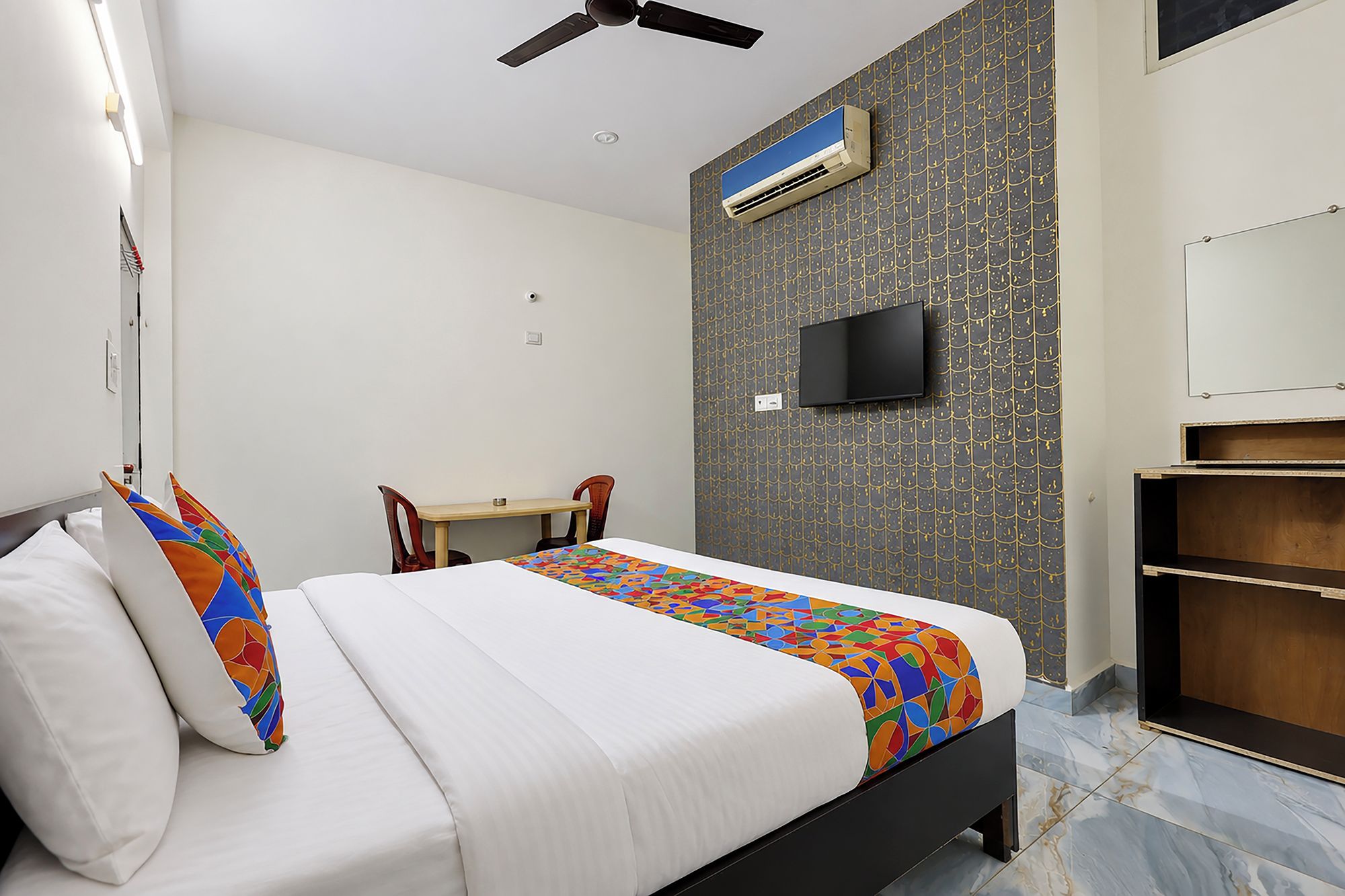 Een hotelkamer met een bed, een bureau, een stoel, een televisie en een airconditioning.
