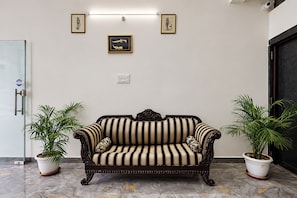 A room with a striped sofa, two potted plants, and framed artwork on the wall.