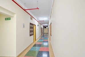 A hallway with a fire exit sign, a door with a decorative grille, and a colorful tiled floor. - FabHotel Apsara (Patna)