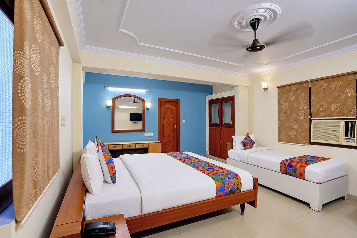 A hotel room with two beds, a ceiling fan, a mirror, and a window with blinds.