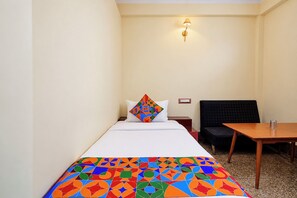 A hotel room with a bed, a colorful geometric-patterned bedspread, a black upholstered bench, a small wooden table, and a wall-mounted light fixture. - FabHotel Apsara (Patna)