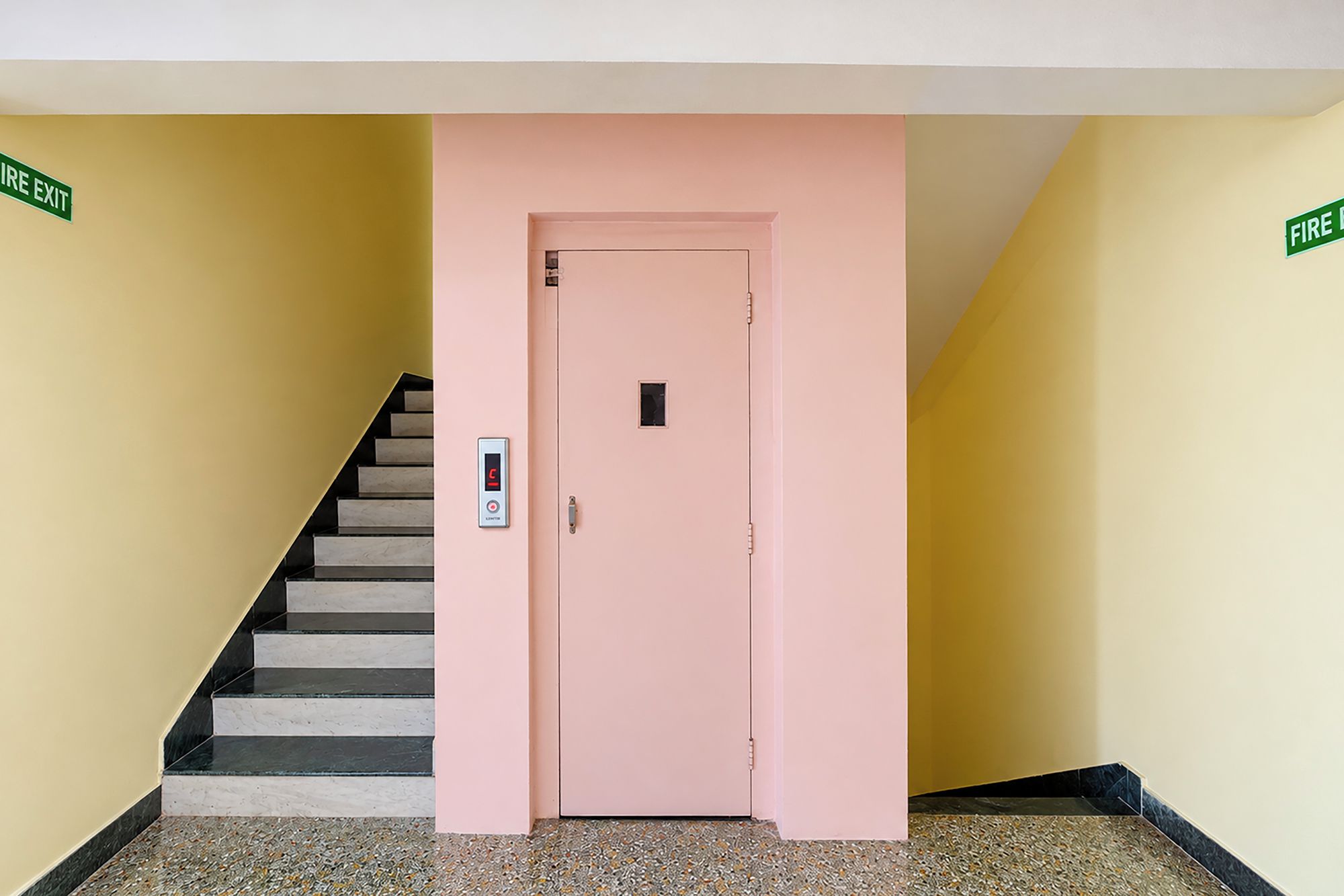 A pink door with a digital lock and a stairwell with a handrail.