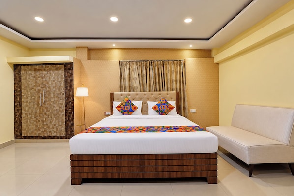 A hotel room with a large bed, a sofa, a lamp, and a wardrobe. - FabHotel Apsara (Patna)