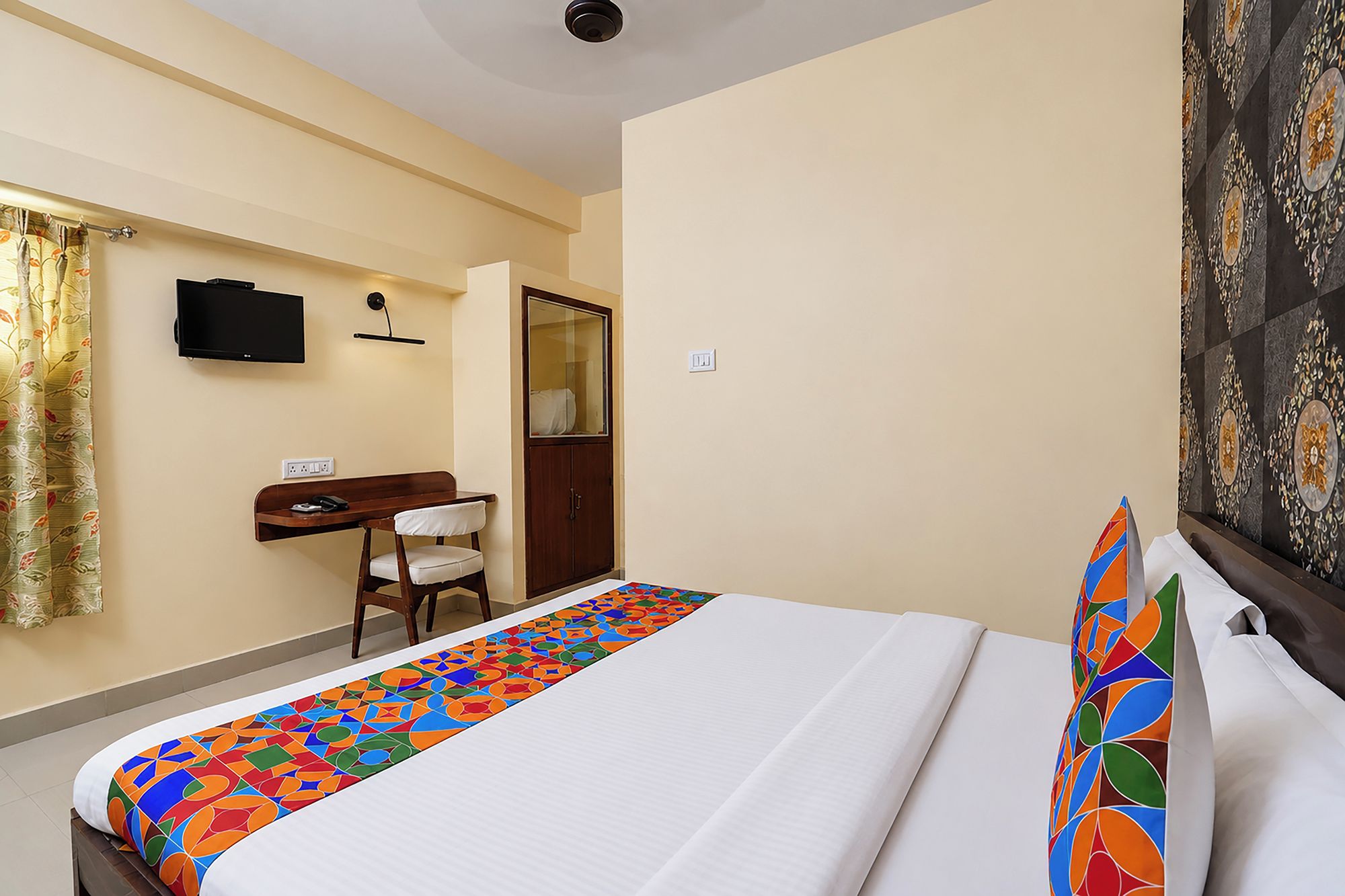 A hotel room with a bed, a desk, a chair, a television, and a patterned curtain.