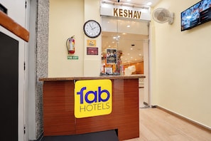 Una recepción de hotel con un reloj, una señal de salida de incendios y un cartel que dice 'Keshav Hotels'.
