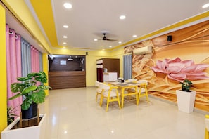 A hotel lobby with a reception desk, a dining area with yellow chairs, and a large floral mural on the wall. - FabHotel Apsara (Patna)