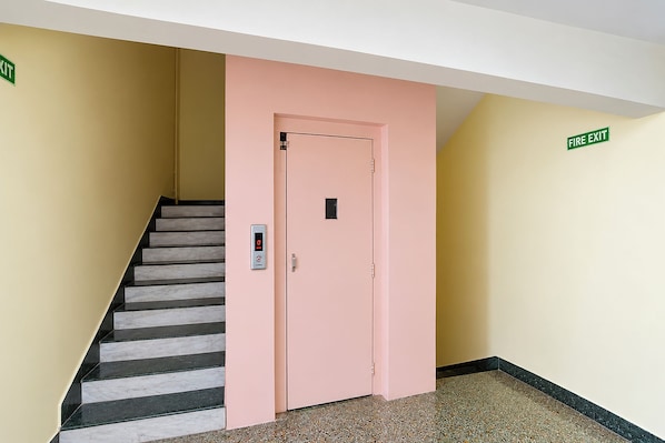A hotel lobby with a pink elevator, a staircase, and a fire exit sign. - FabHotel Apsara (Patna)