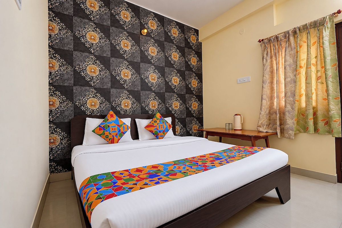 A bed with a colorful geometric-patterned bedspread, a dark headboard with decorative panels, and a window with a floral curtain.