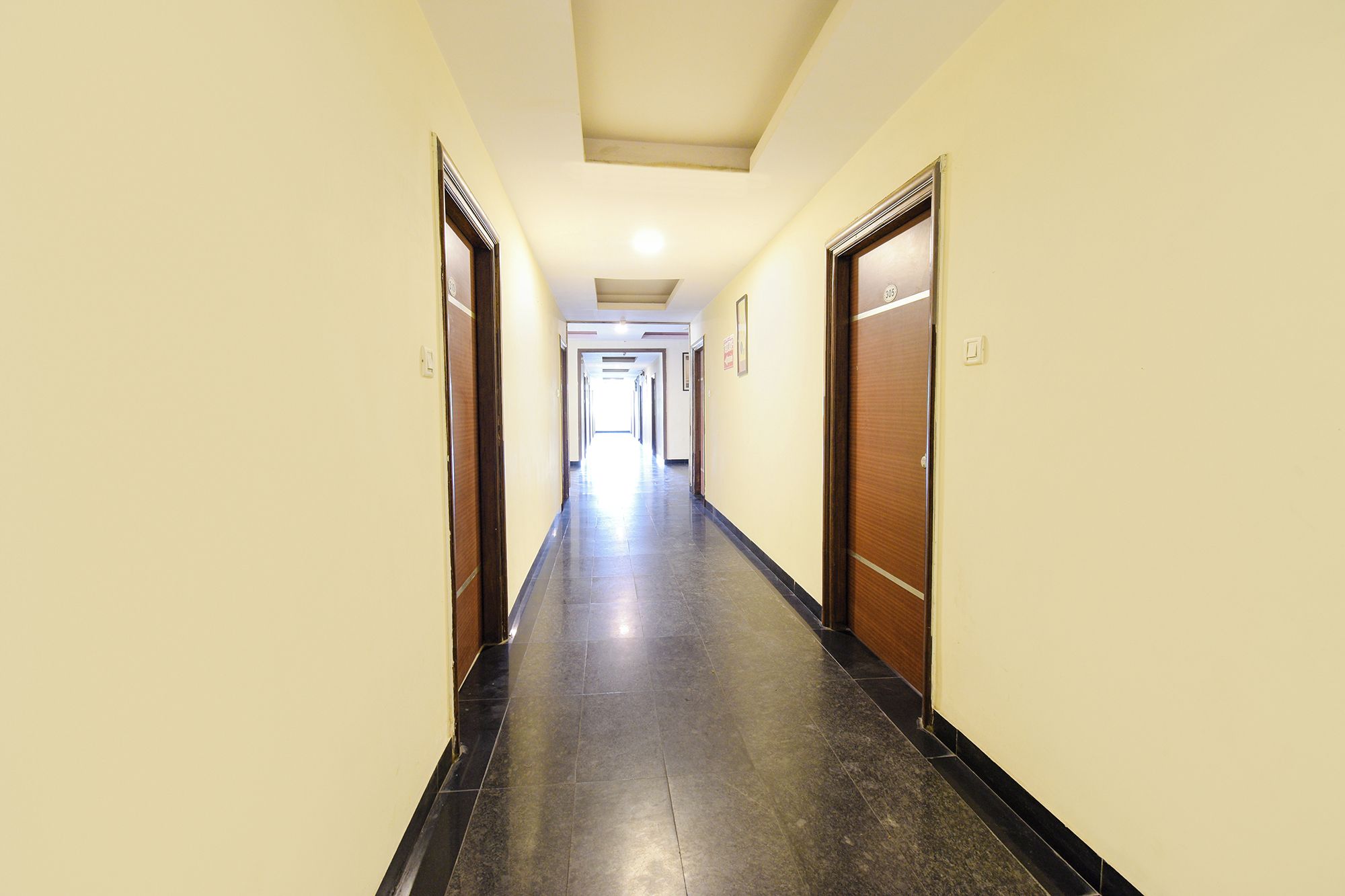 Un pasillo de hotel con puertas a ambos lados, piso de baldosas y una lámpara en el techo.