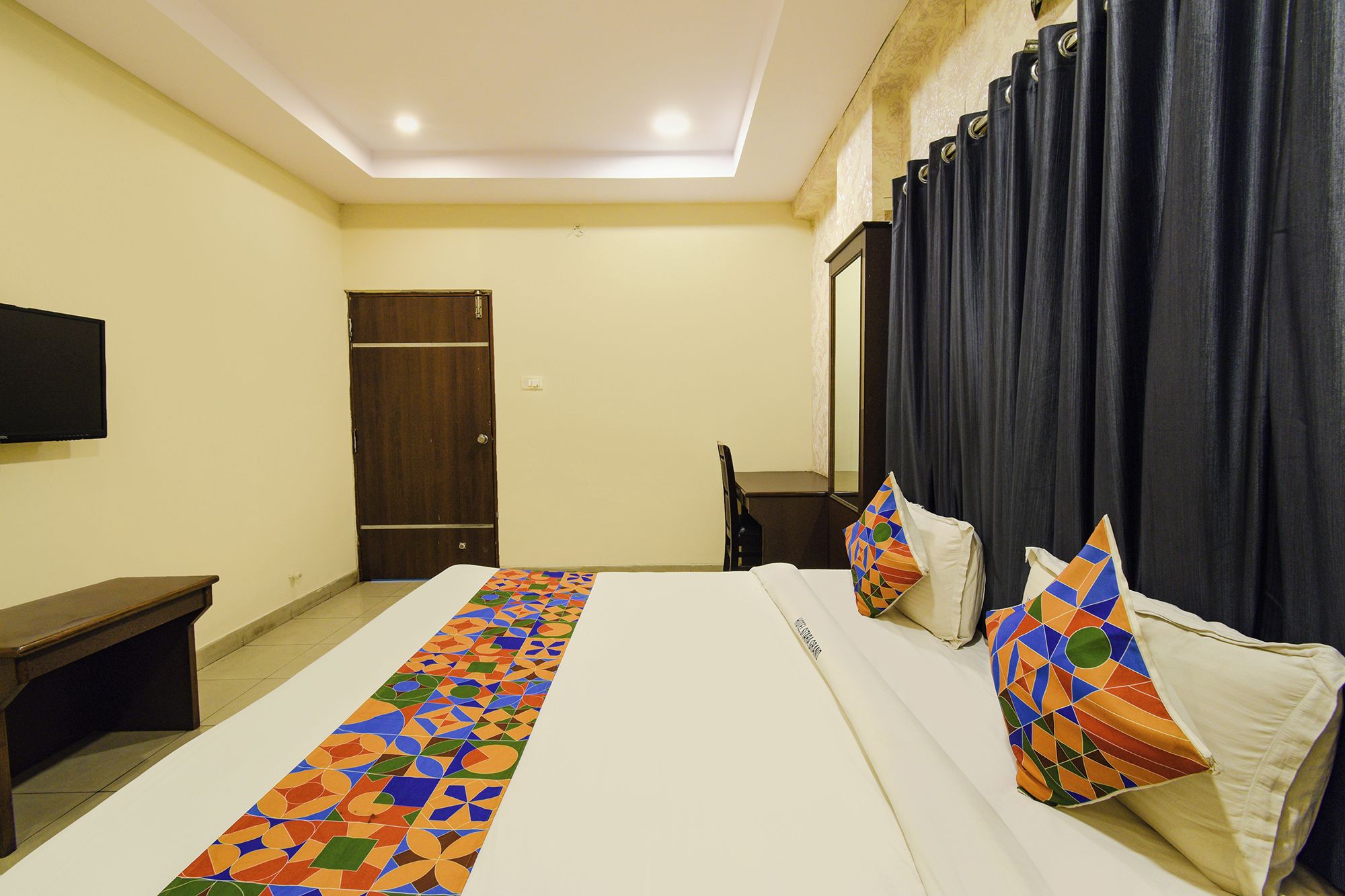 A hotel room with a bed, a desk, a chair, a TV, and a door.