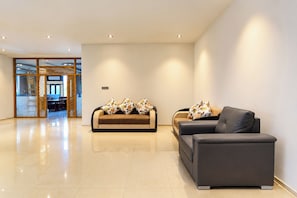 Un espacio moderno con dos sofás y una mesa de comedor, un separador de madera y una puerta de cristal que da a otra habitación.