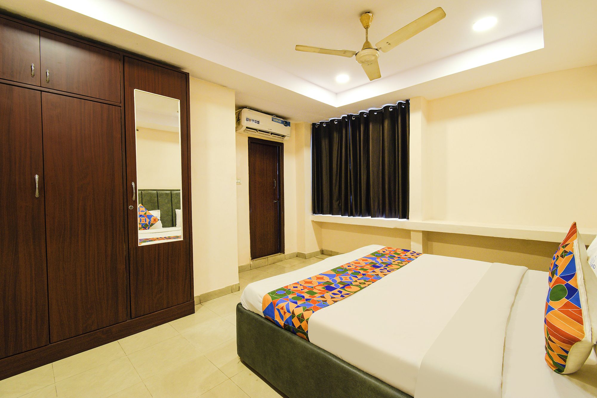 A bedroom with a bed, wardrobe, mirror, ceiling fan, and air conditioning unit.