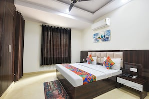 A hotel room with a bed, bedside table, nightstand, and an air conditioning unit. - FabHotel Swastik Anand Vihar (New Delhi)
