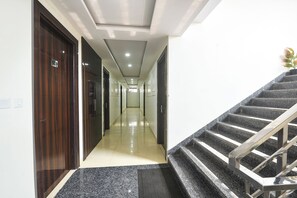 Un couloir d’hôtel avec un sol recouvert de moquette, une porte en bois sur la gauche et un escalier sur la droite.