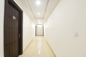 Un long couloir étroit aux murs blancs, avec une porte en bois sur le côté gauche.
