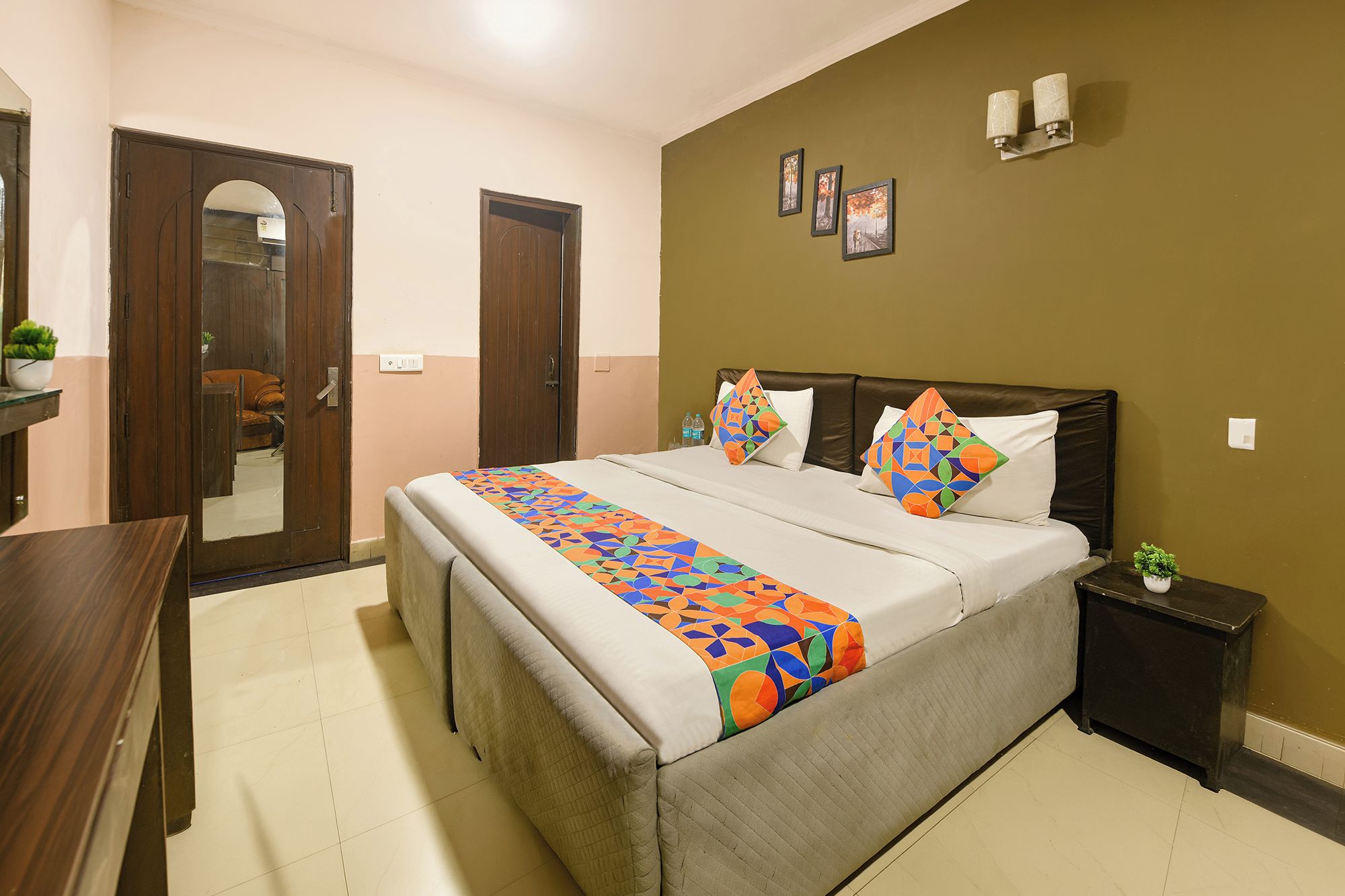 Une chambre d’hôtel avec un lit, une table de chevet, une commode, un miroir et une porte.