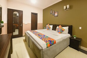 A hotel room with a bed, a bedside table, a nightstand, a mirror, and a door. - FabHotel The Royal Galaxy (New Delhi)
